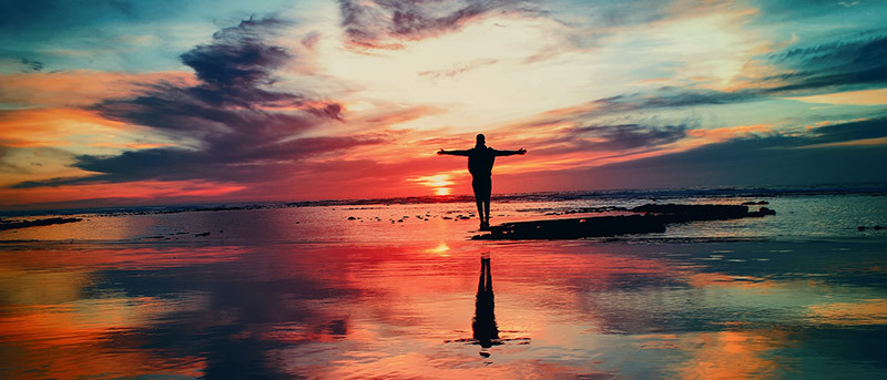 Silhouette of person standing in front of sunset with outstretched arms